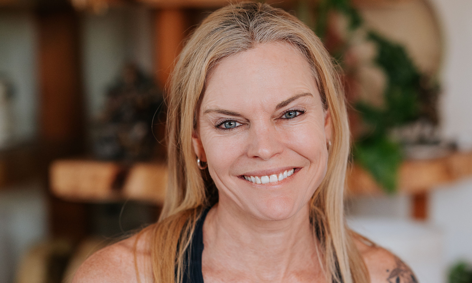 Experienced yoga instructor with a confident gaze and hands gently placed on heart, wearing a sleeveless top and showcasing her arm tattoo, representing the blend of strength and grace at Shala Yoga studio in Squamish.