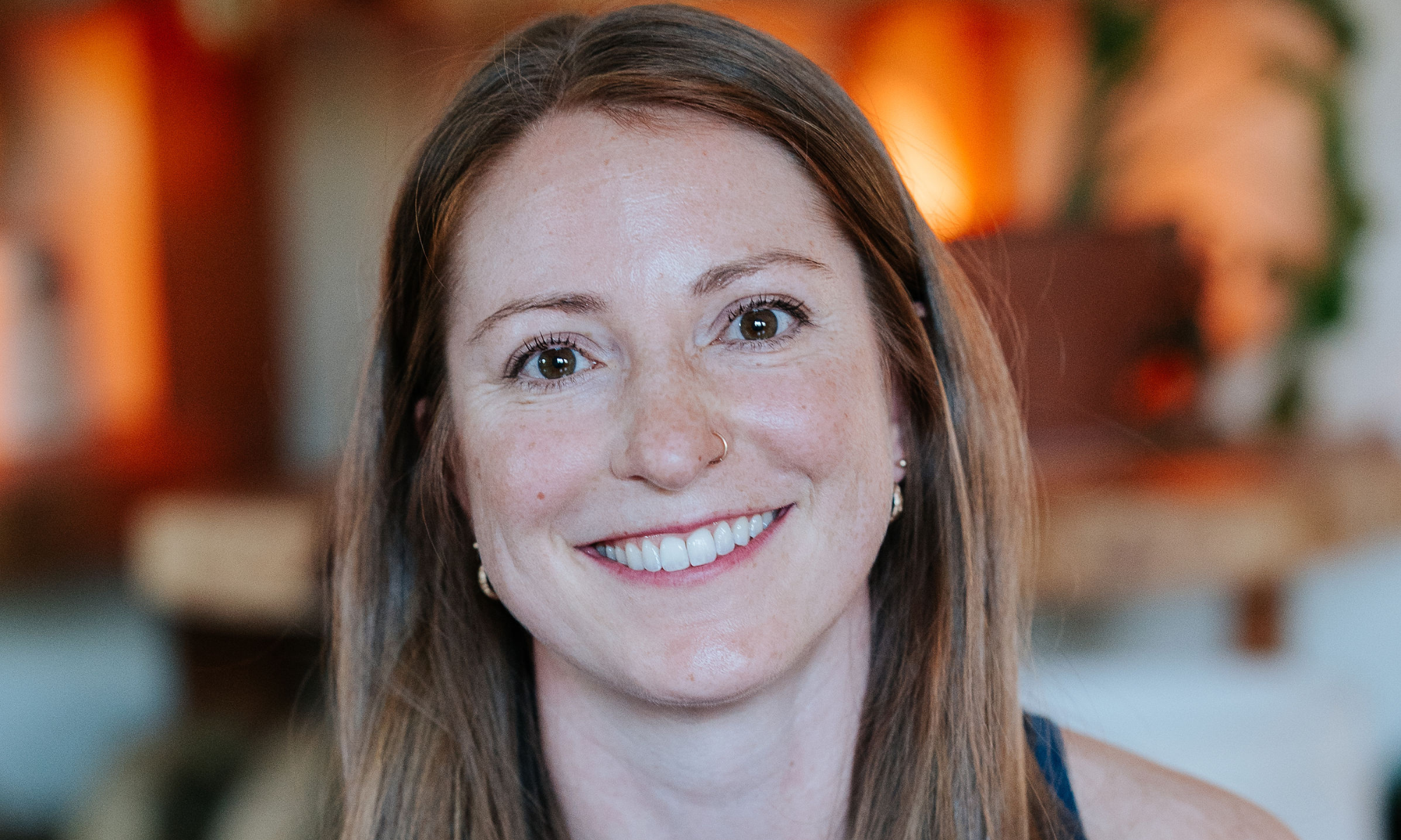 Portrait of a smiling yoga instructor with warm, welcoming expression, wearing a blue top, showcasing a casual and friendly vibe at Shala Yoga studio in Squamish, symbolizing the studio's approachable and supportive community atmosphere.