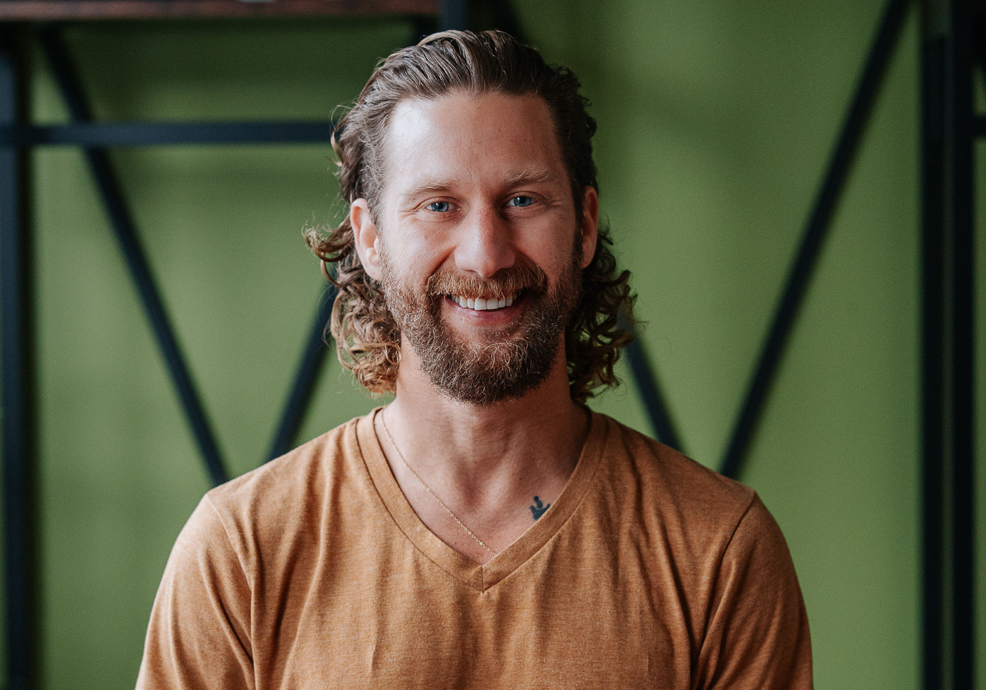Energetic and friendly male yoga instructor with a beard, wearing a sleeveless dark tank top and a warm smile, epitomizing the inviting and positive energy at Shala Yoga studio in Squamish.