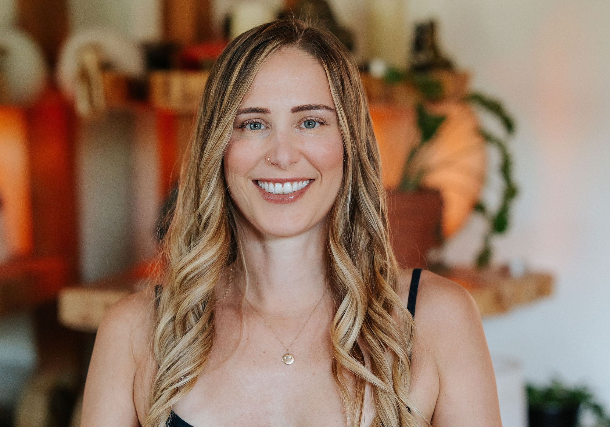 Warm and welcoming yoga instructor with a gentle smile, wearing a simple black top, representing the accessible and friendly environment of Shala Yoga studio in Squamish.