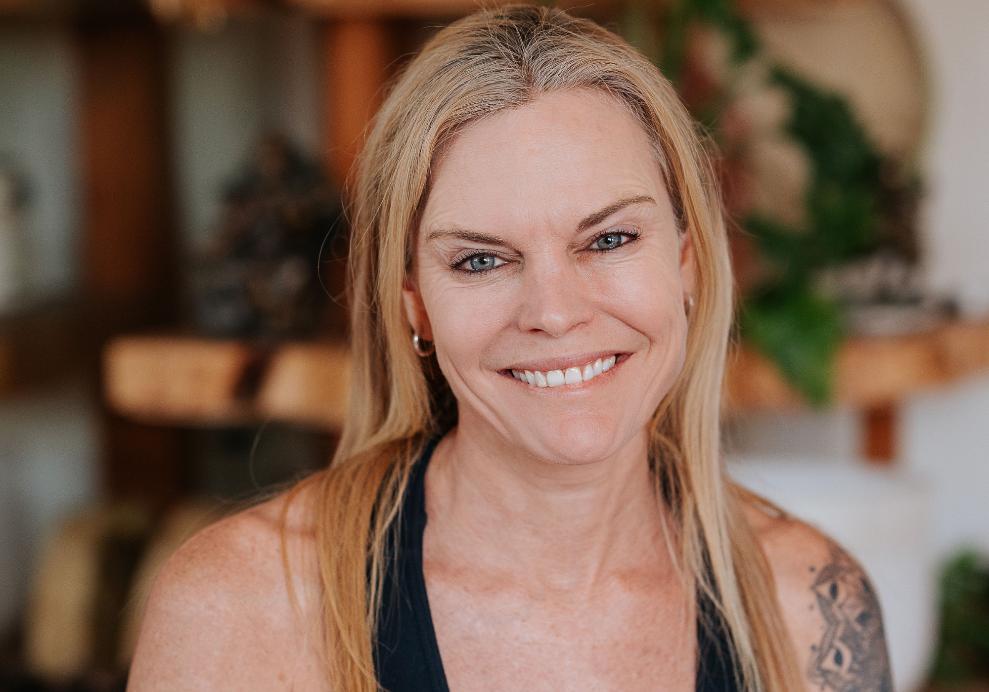 Experienced yoga instructor with a confident gaze and hands gently placed on heart, wearing a sleeveless top and showcasing her arm tattoo, representing the blend of strength and grace at Shala Yoga studio in Squamish.