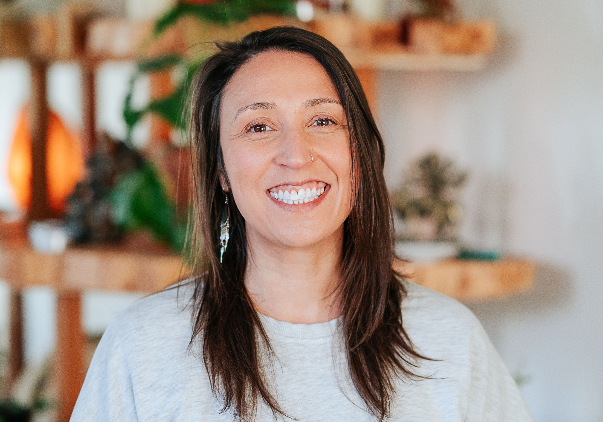 Warm and welcoming yoga instructor with a gentle smile, wearing a simple black top, representing the accessible and friendly environment of Shala Yoga studio in Squamish.
