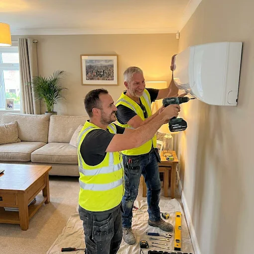 Thomas and Ledion installing an indoor unit in a living room