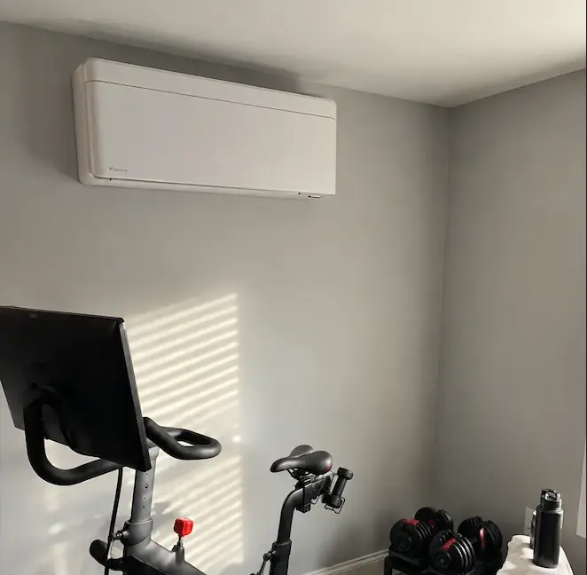 A Daikin wall unit in a home gym, above a Peloton bike and free weights