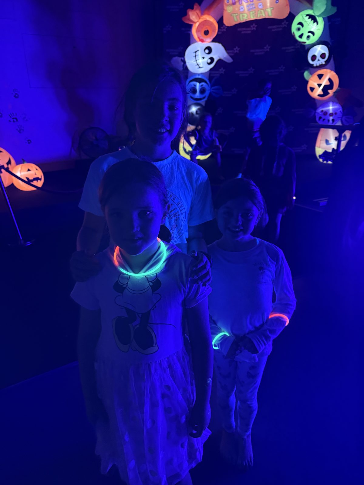 Kids wearing glow necklaces under UV light by the glowing Halloween arch