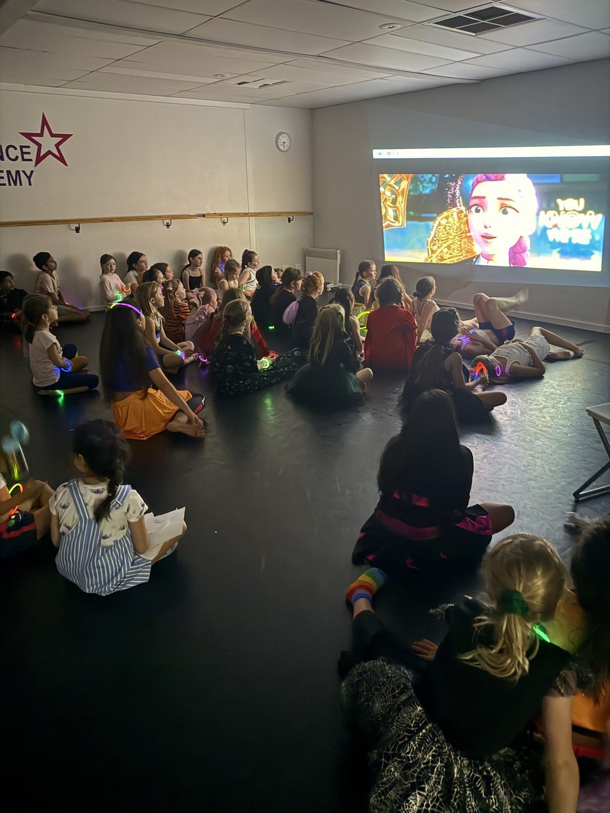Kids in costume sitting together on the studio floor watching a movie on the big screen