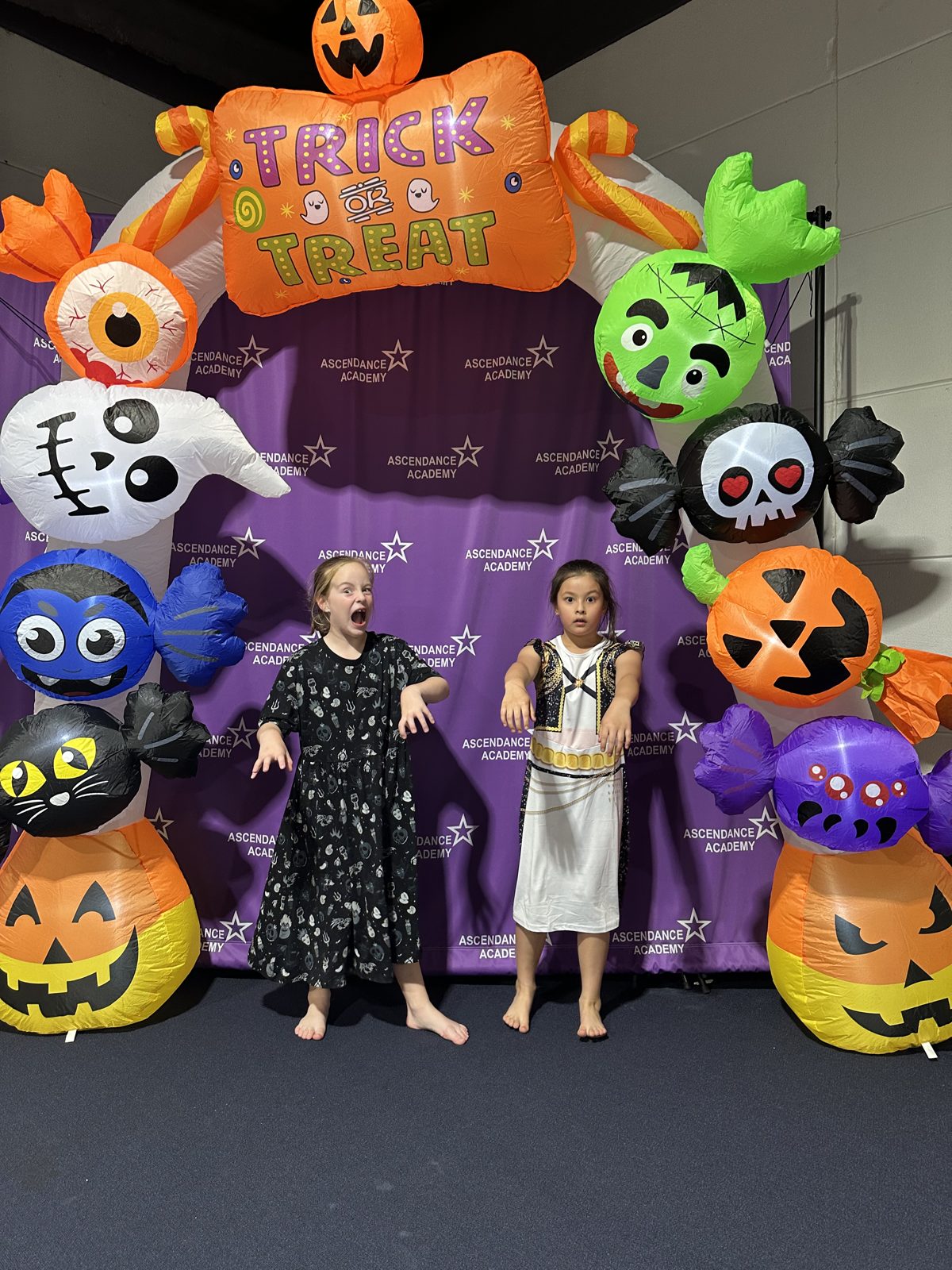 Two kids in costume doing spooky poses under the Trick or Treat arch