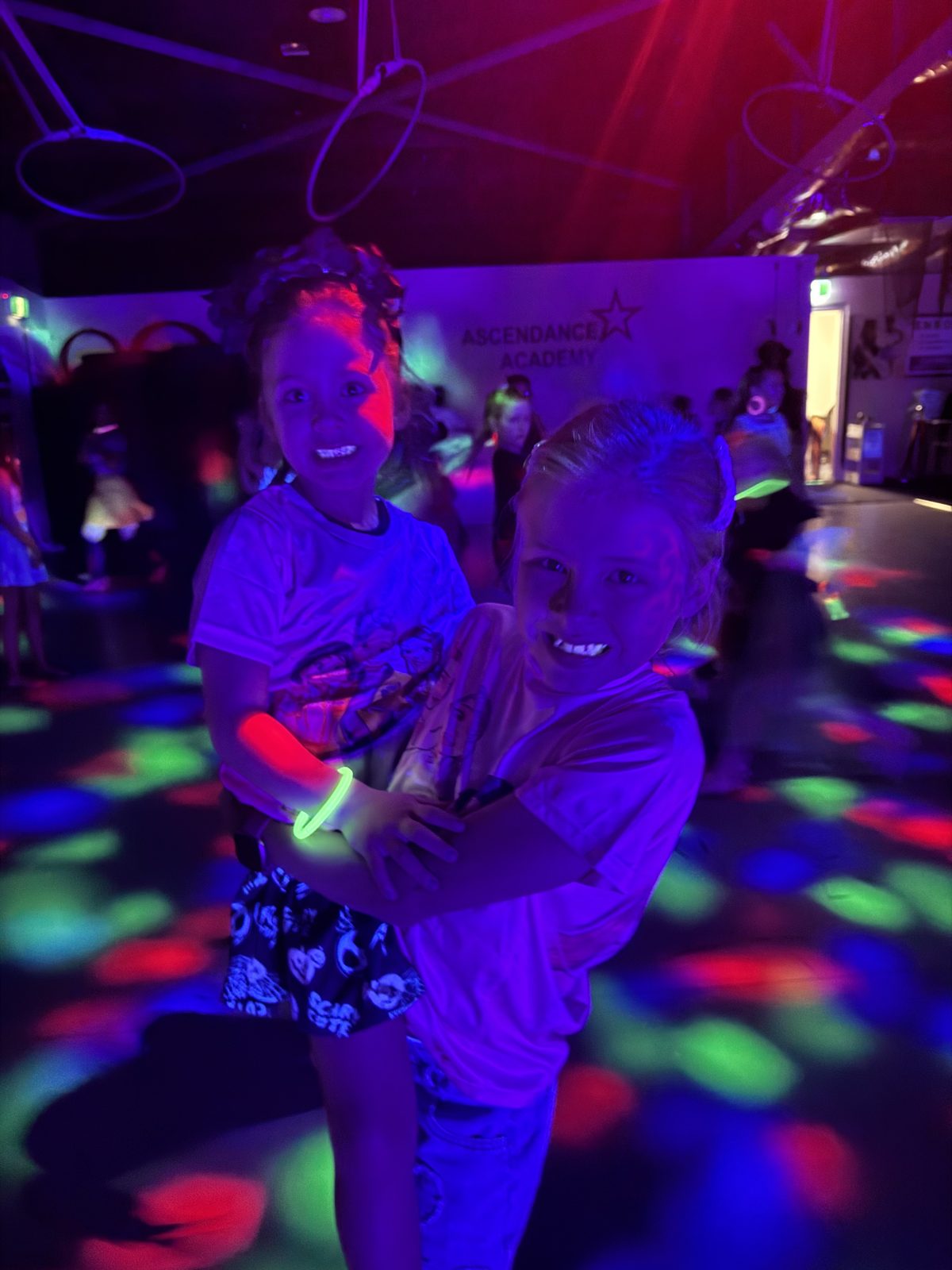 Two kids with glow bracelets hugging and laughing on the disco dance floor