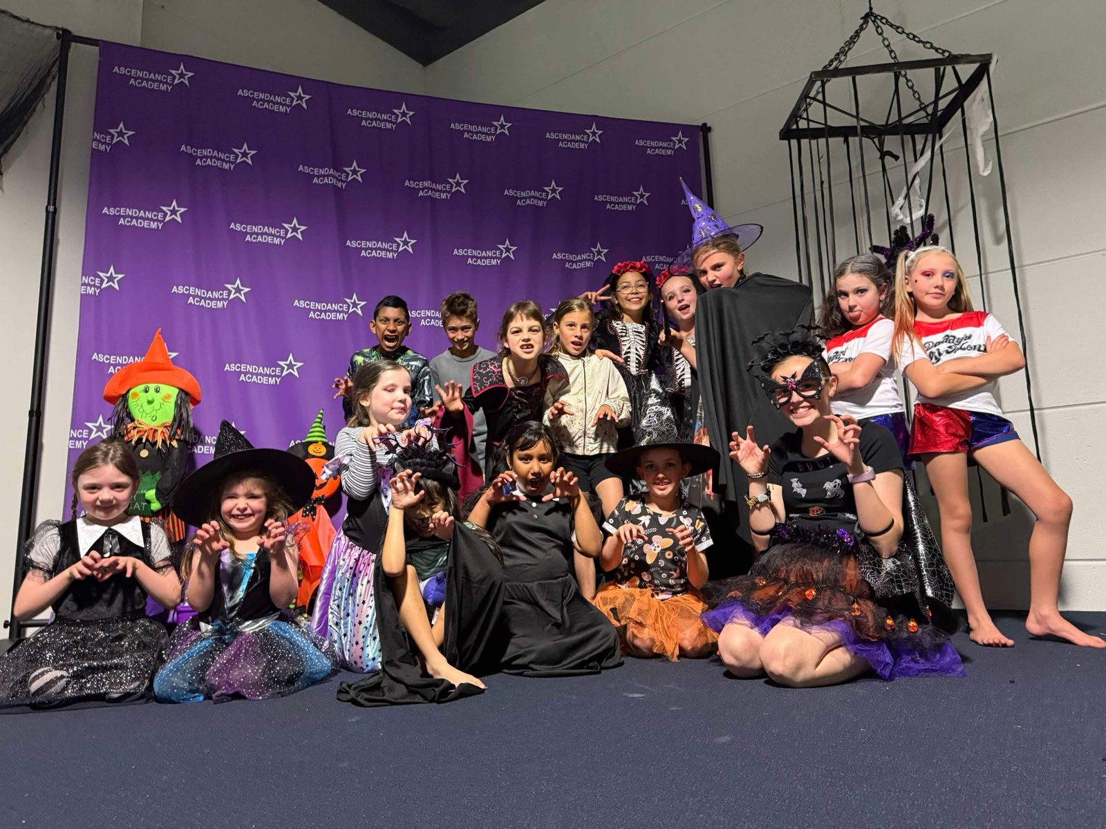 A big group of kids in Halloween costumes pulling monster poses in front of the Ascendance Academy backdrop