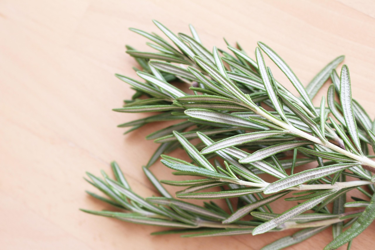 A bundle of fresh rosemary on a pale wooden table.