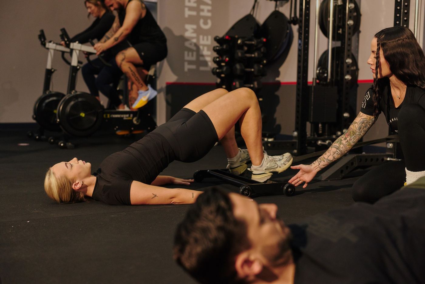 F45 coach coaching a member through glute bridges on the floor