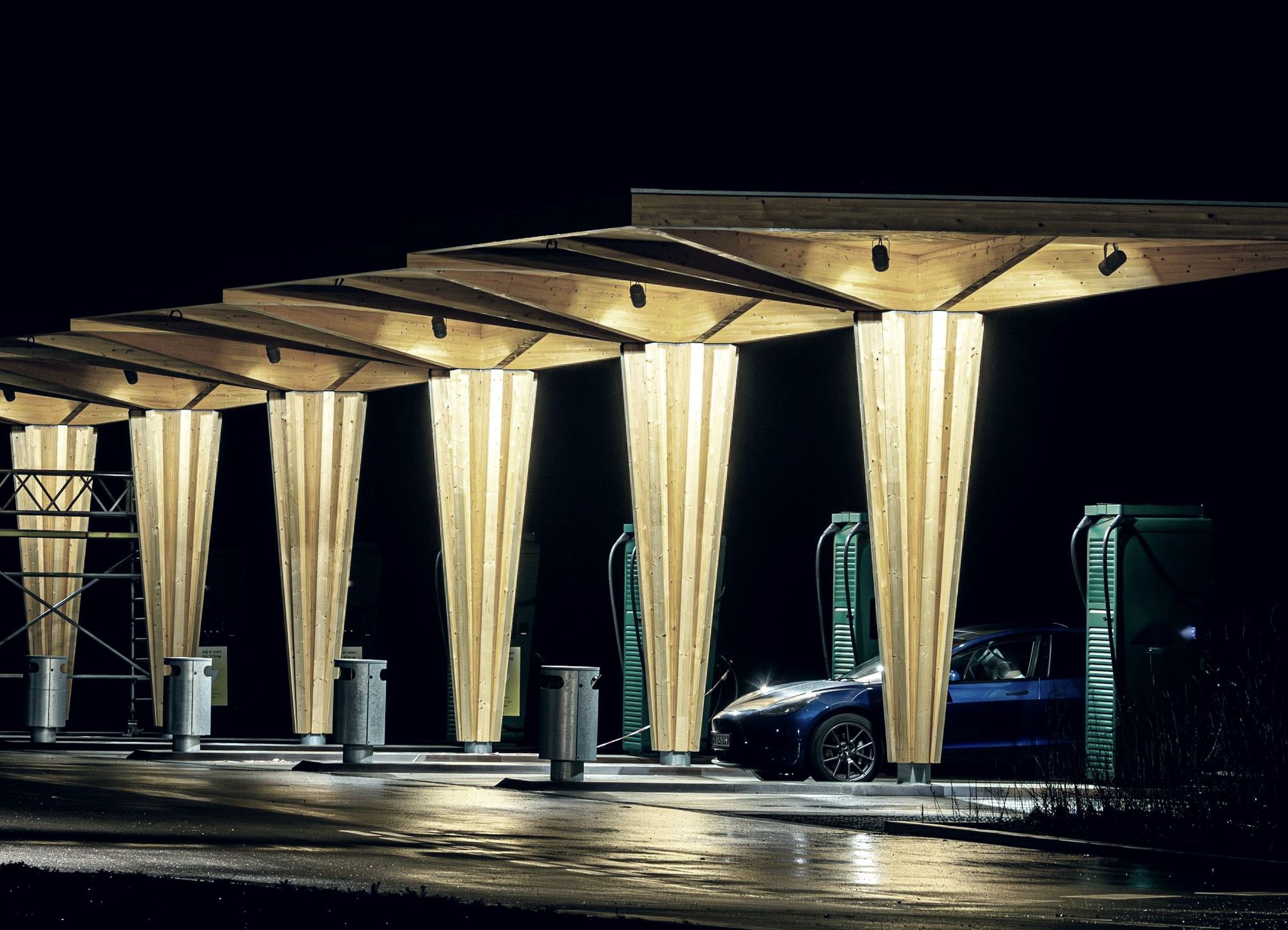 DC fast chargers under a lit timber canopy at night