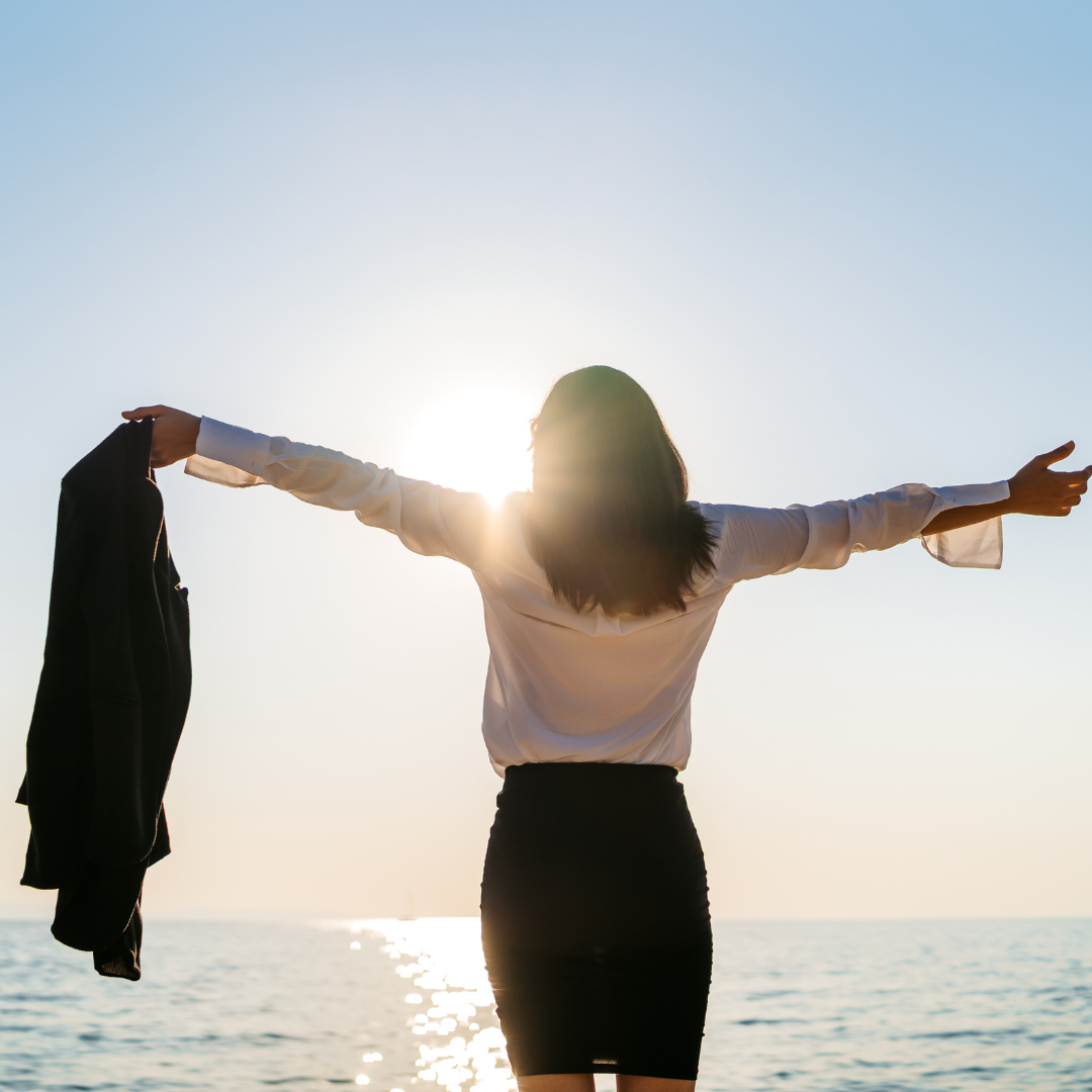Woman in business attire standing at the ocean's edge with arms outstretched toward the sunrise Woman in business attire standing at the ocean's edge with arms outstretched toward the sunrise