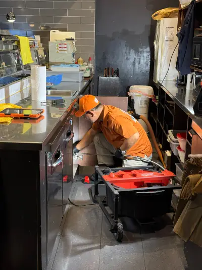 Technician repairing drain lines in a commercial kitchen