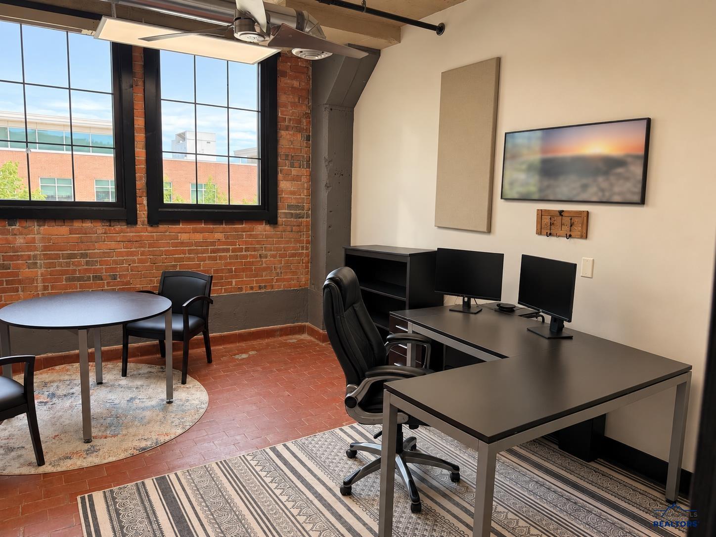 Private office in Suite 201 with exposed brick and large windows (shown with current tenant furnishings)