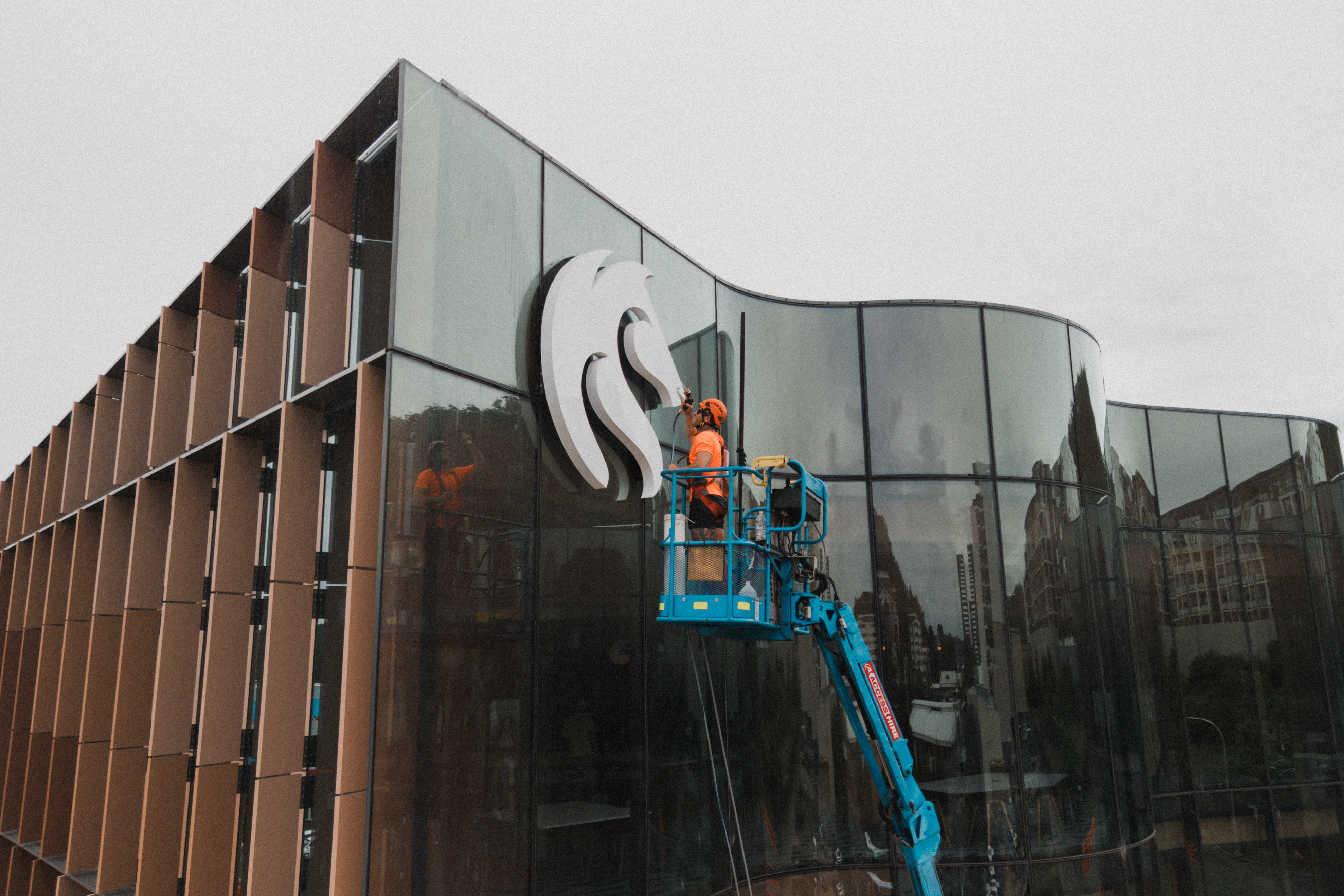 Operator on elevated work platform cleaning signage and glass on a modern school building