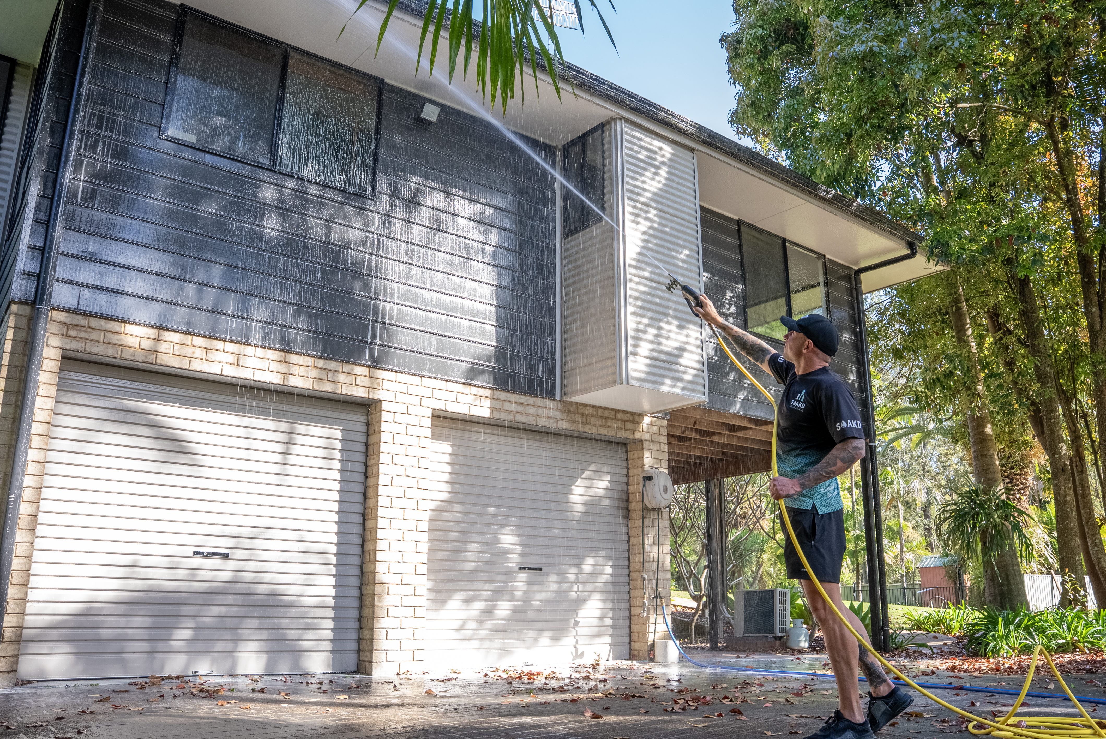 SOAKD operator softwashing the exterior walls of a two-storey coastal residential home