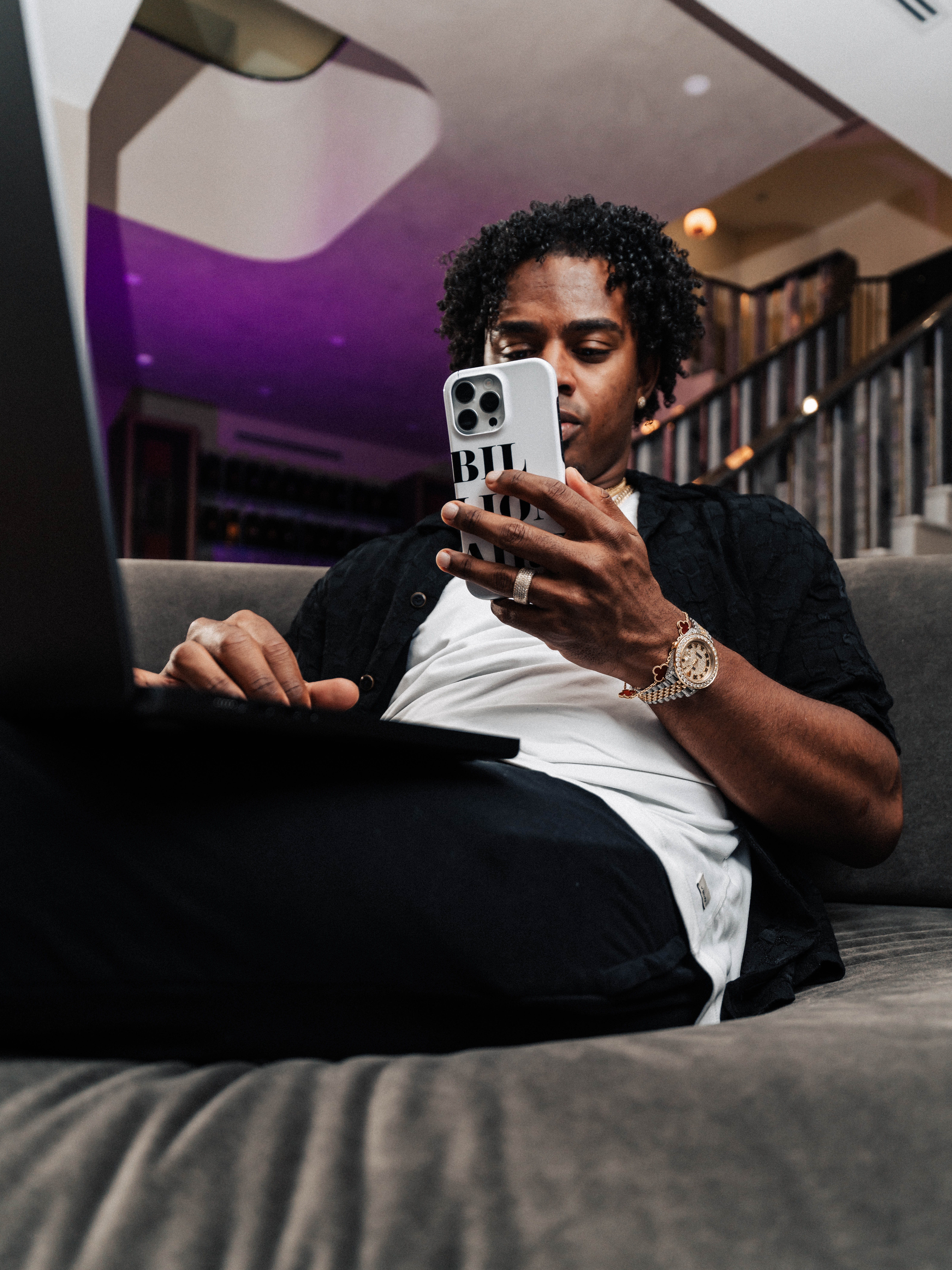 Working from the couch, laptop open and phone in hand.