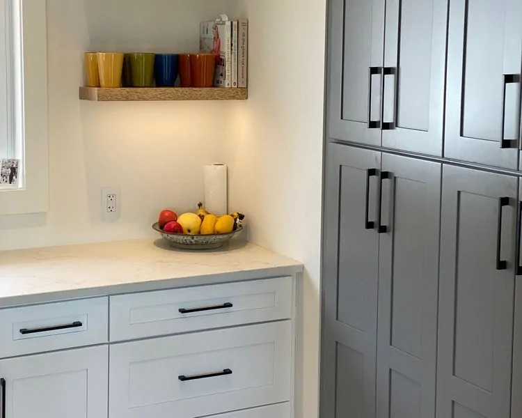 In-stock gray shaker pantry cabinets with a fruit bowl and colourful mugs on an open wood shelf