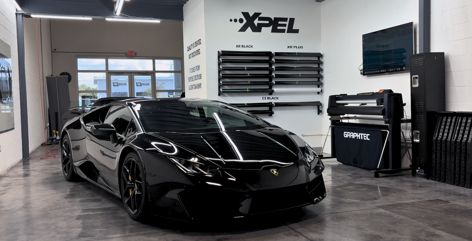 A black Lamborghini Huracan inside the Mission Tint shop, in front of the XPEL film wall