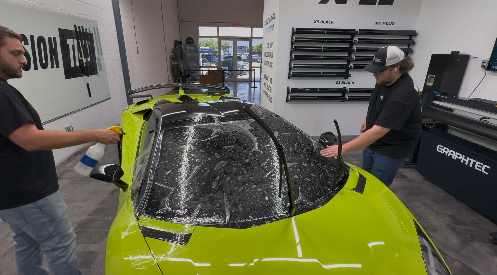 Two Mission Tint installers applying protection film to the windshield of a green supercar