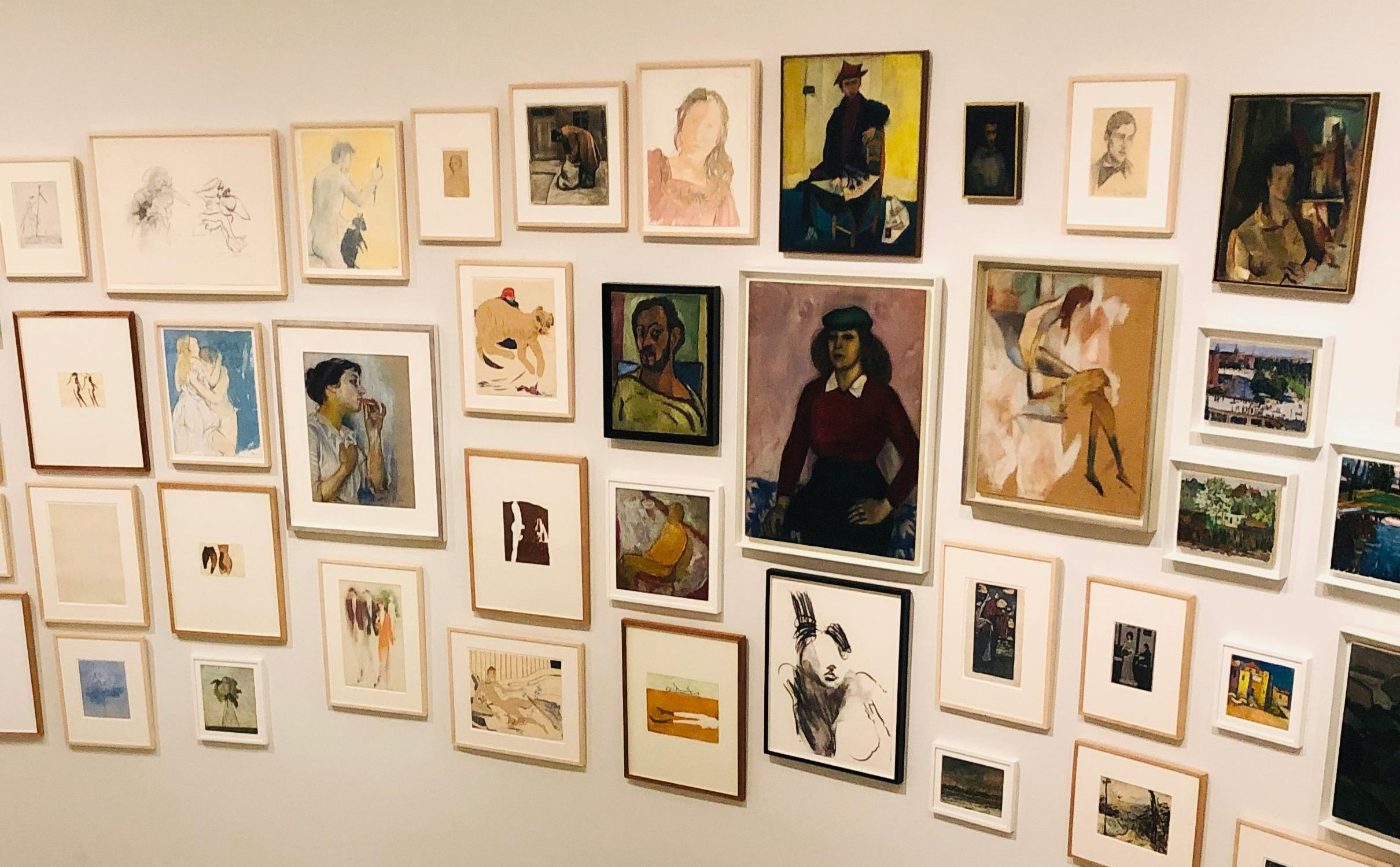 An eclectic, salon-style gallery wall featuring a curated collection of framed portraits, sketches, and paintings arranged closely together on a white wall. An eclectic, salon-style gallery wall featuring a curated collection of framed portraits, sketches, and paintings arranged closely together on a white wall.