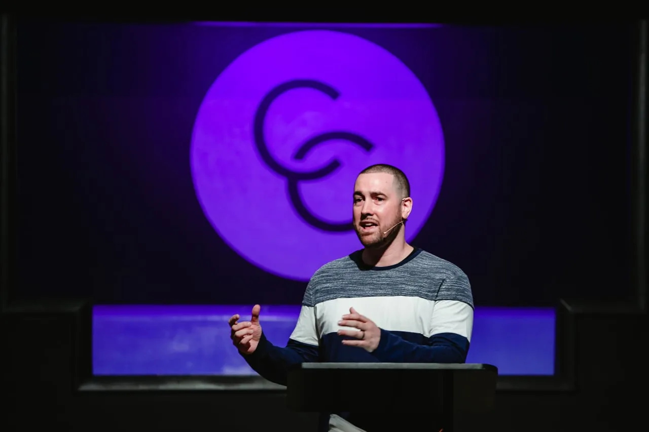 A man speaks into a headset microphone at a lectern in front of a lit Connect Church logo.