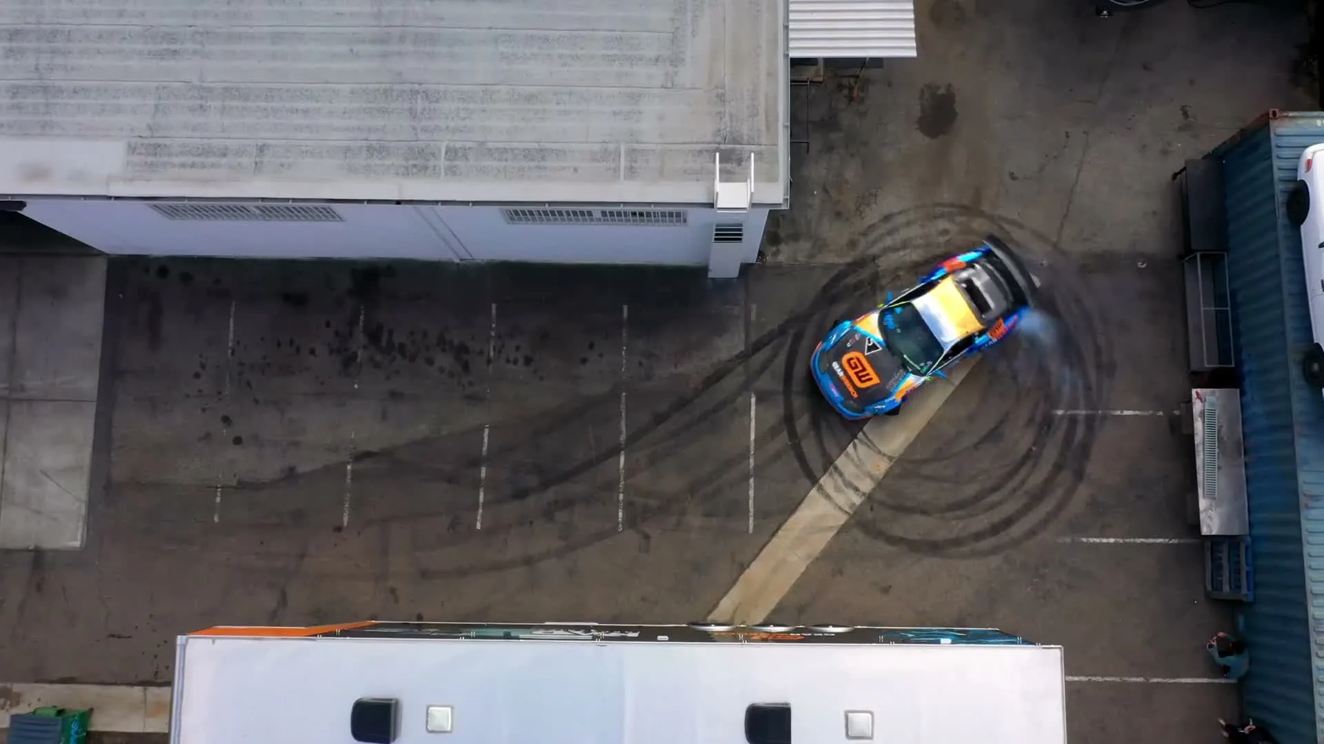 A blue GEARWRENCH-branded car drifts through an industrial yard, seen from above.
