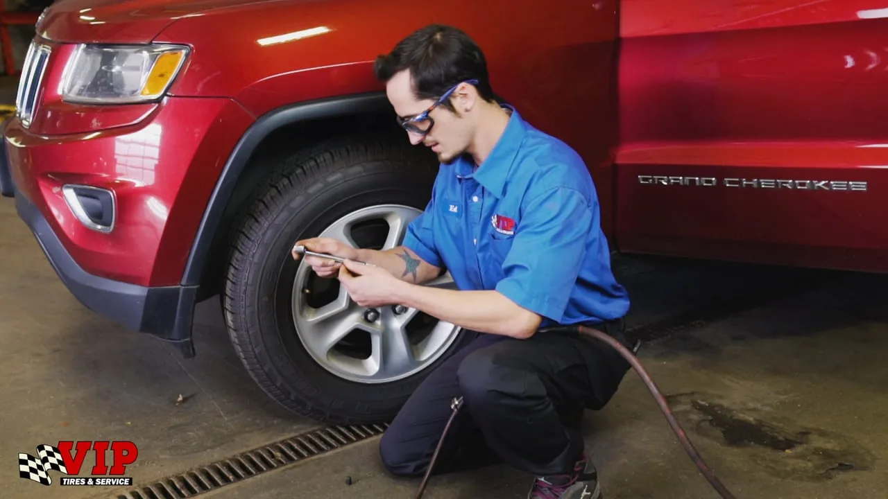 A VIP technician kneels beside a red Jeep in the service bay to check a tire.