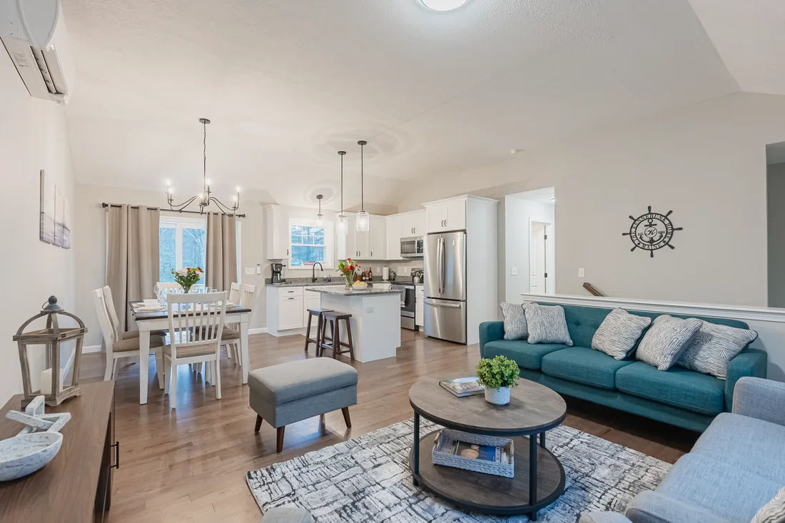 Open plan living room with a teal sofa, dining area and white kitchen beyond, staged and bright