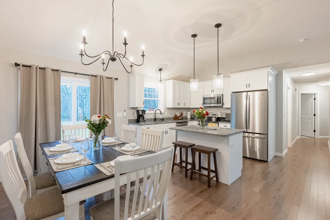 Dining table set with flowers under a wrought iron chandelier, with a white kitchen beyond