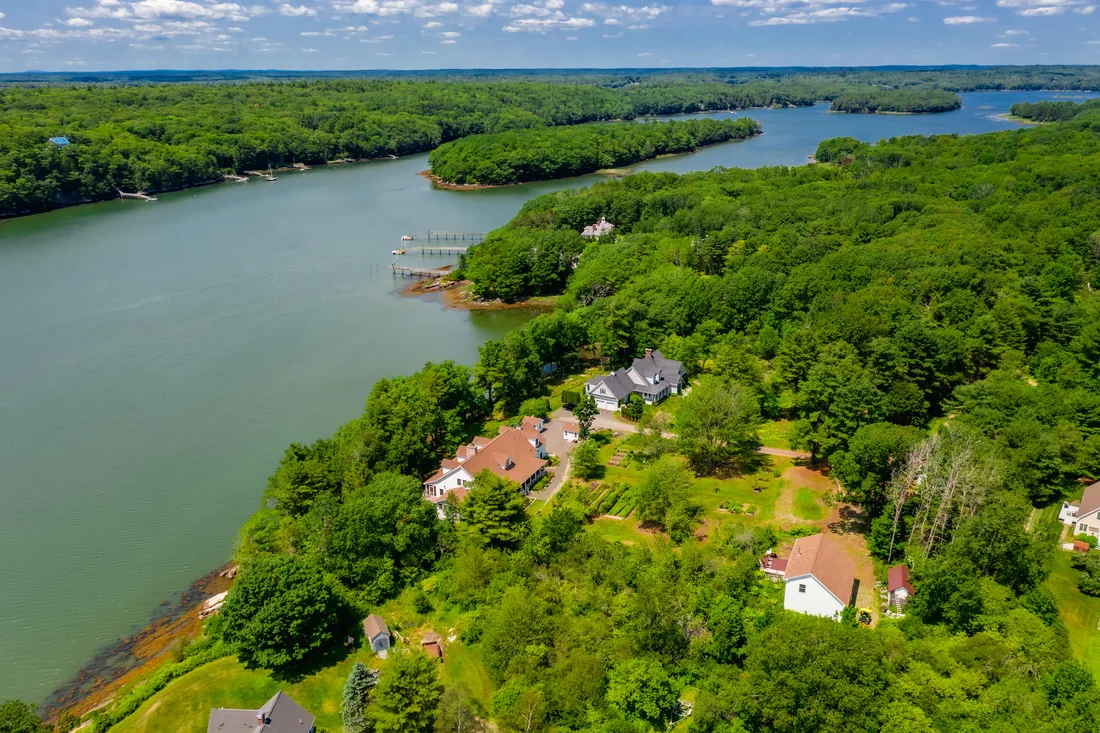 High aerial view of a winding tidal river with wooded islands and private docks, with a waterfront estate and gardens on the near shore