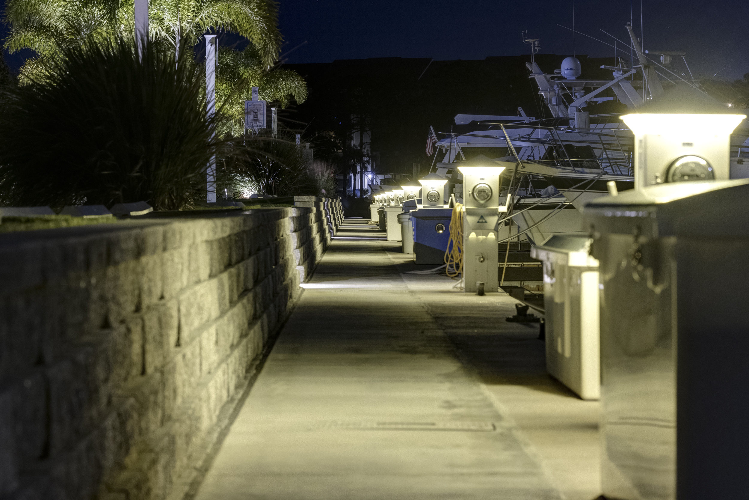 A lit stone walkway between low walls, leading from the parking area toward the docks at night