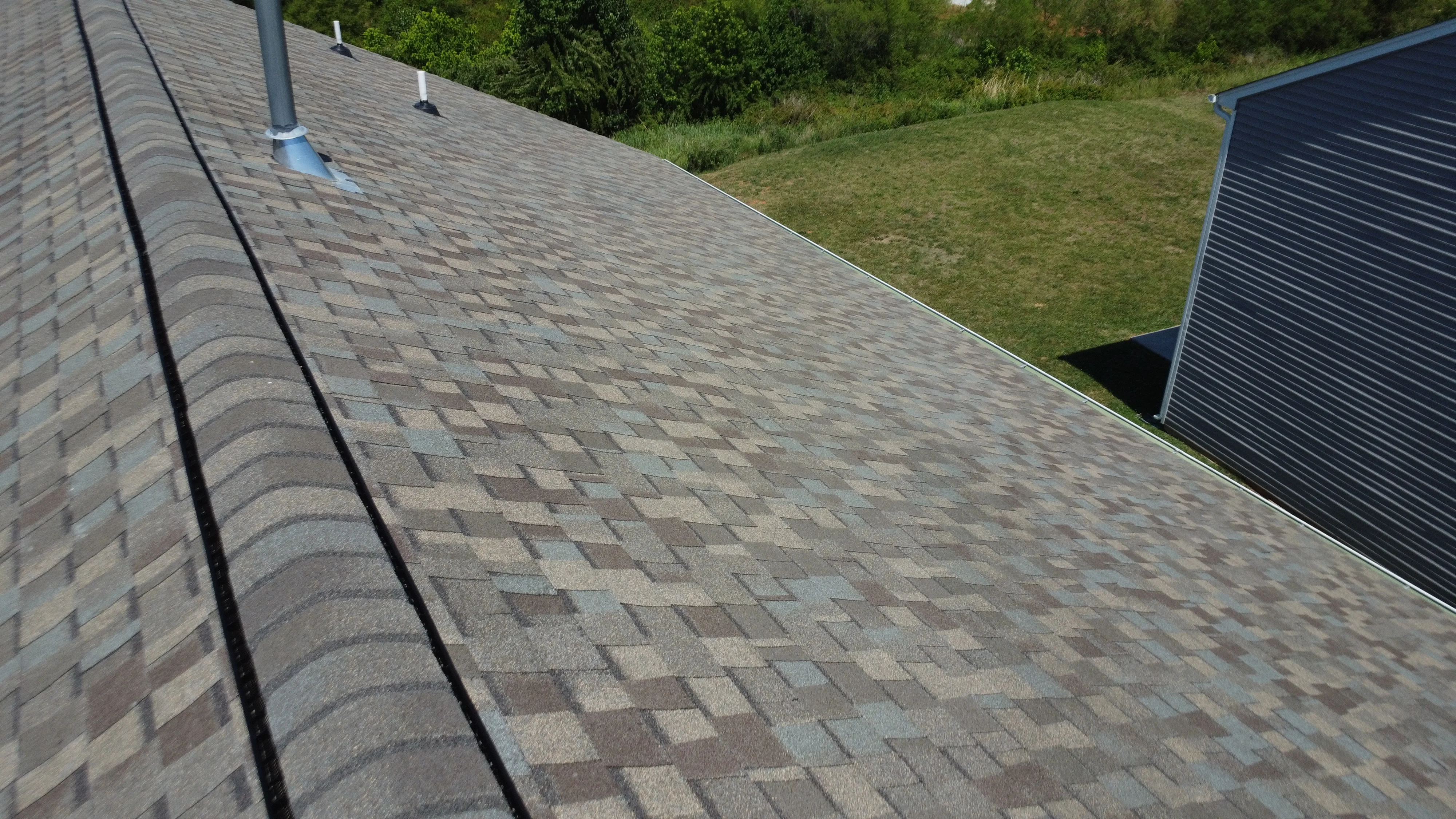 An overhead view of a multi-toned shingle roof with visible ridge vents and two small white pipe vents.