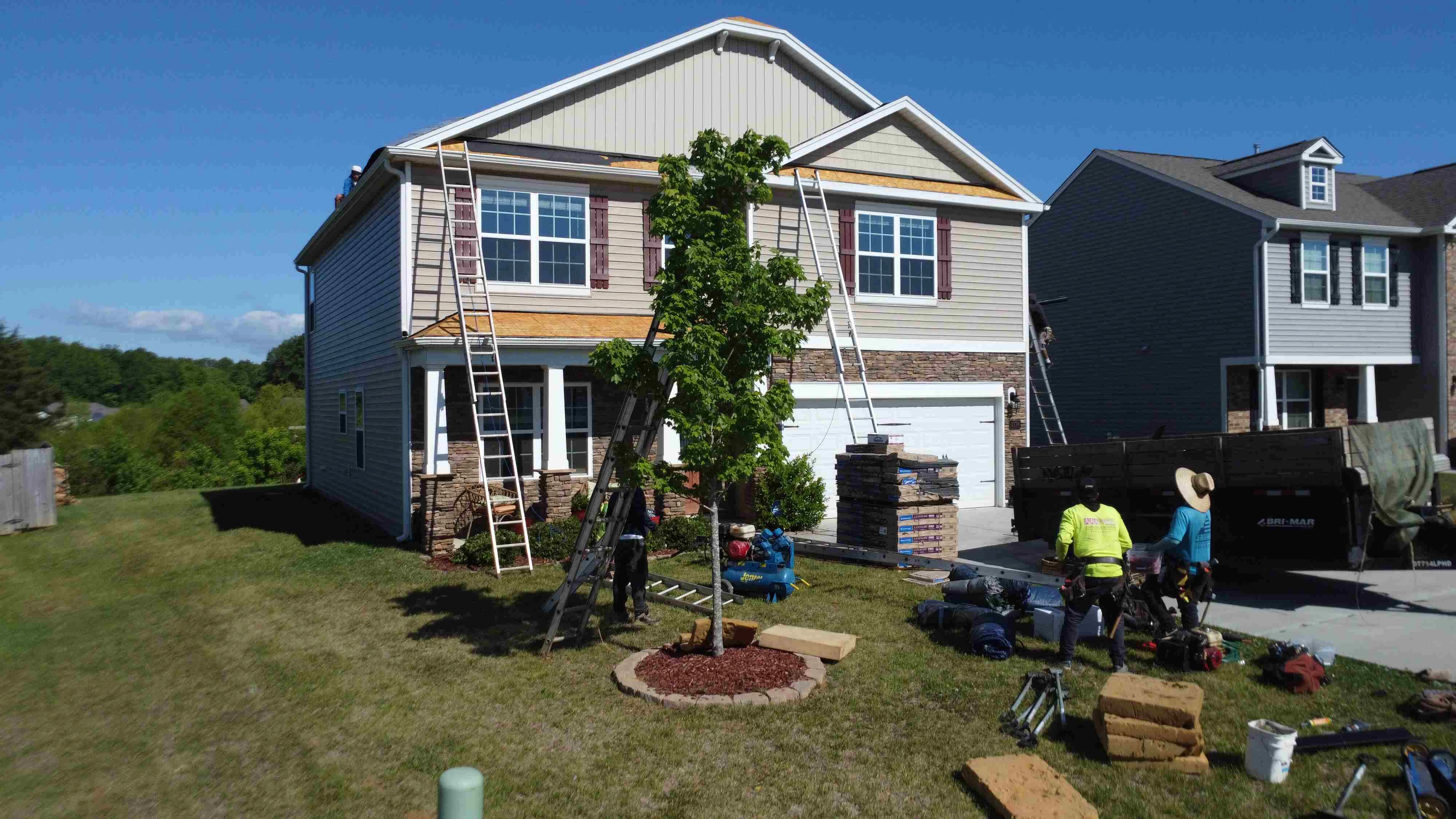 Professional roofing contractors replacing a residential roof on a two-story house, using ladders and roofing materials during a home exterior renovation project.