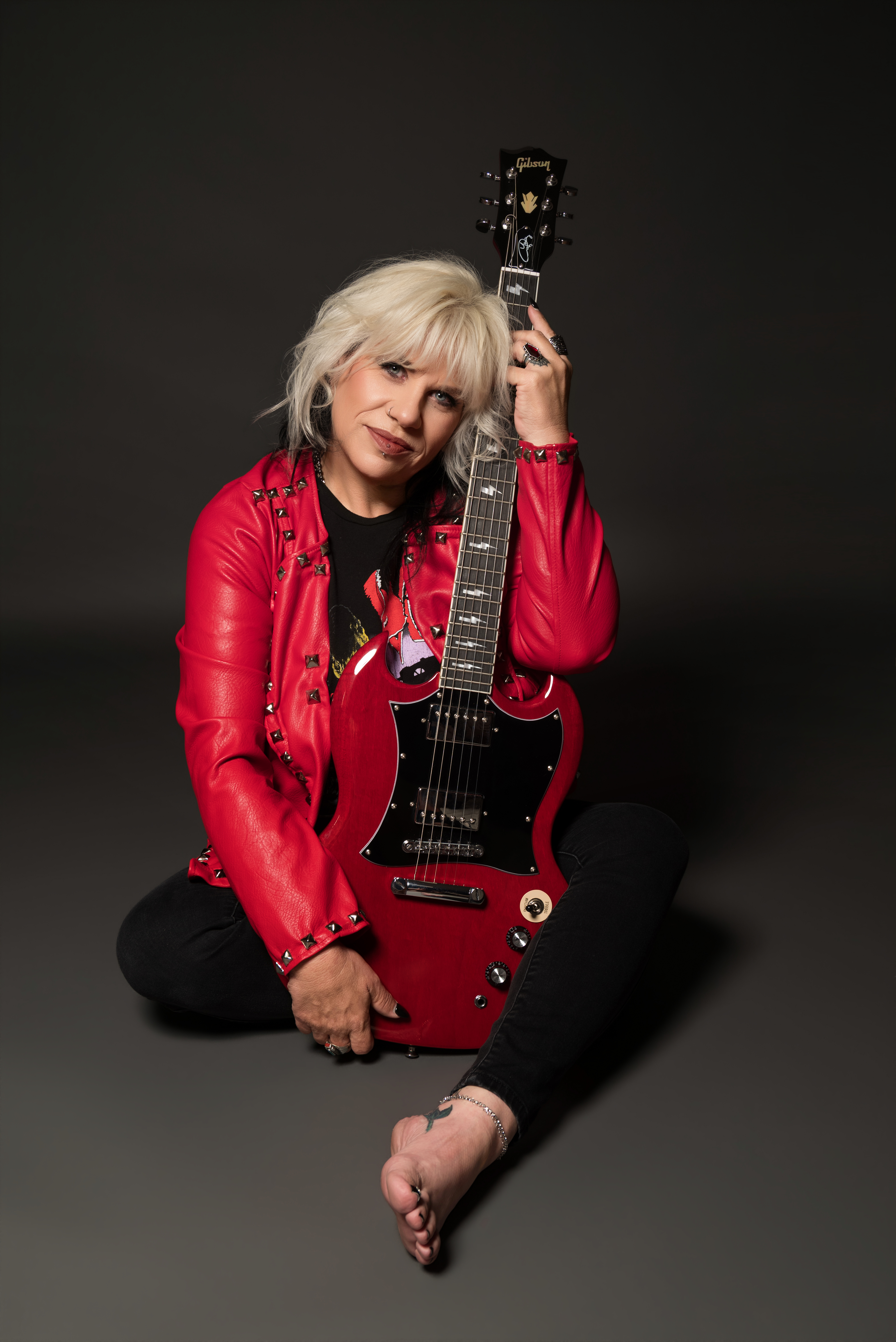 Empowered woman in dark edgy wardrobe holding borrowed guitar with moody stage lighting