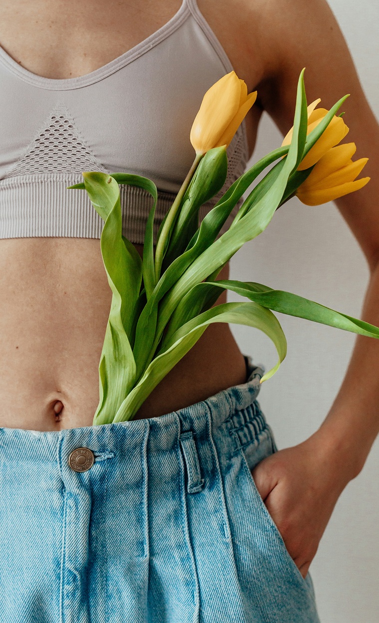 Woman in a light pink bra and blue jeans with yellow tulips in her waist pocket