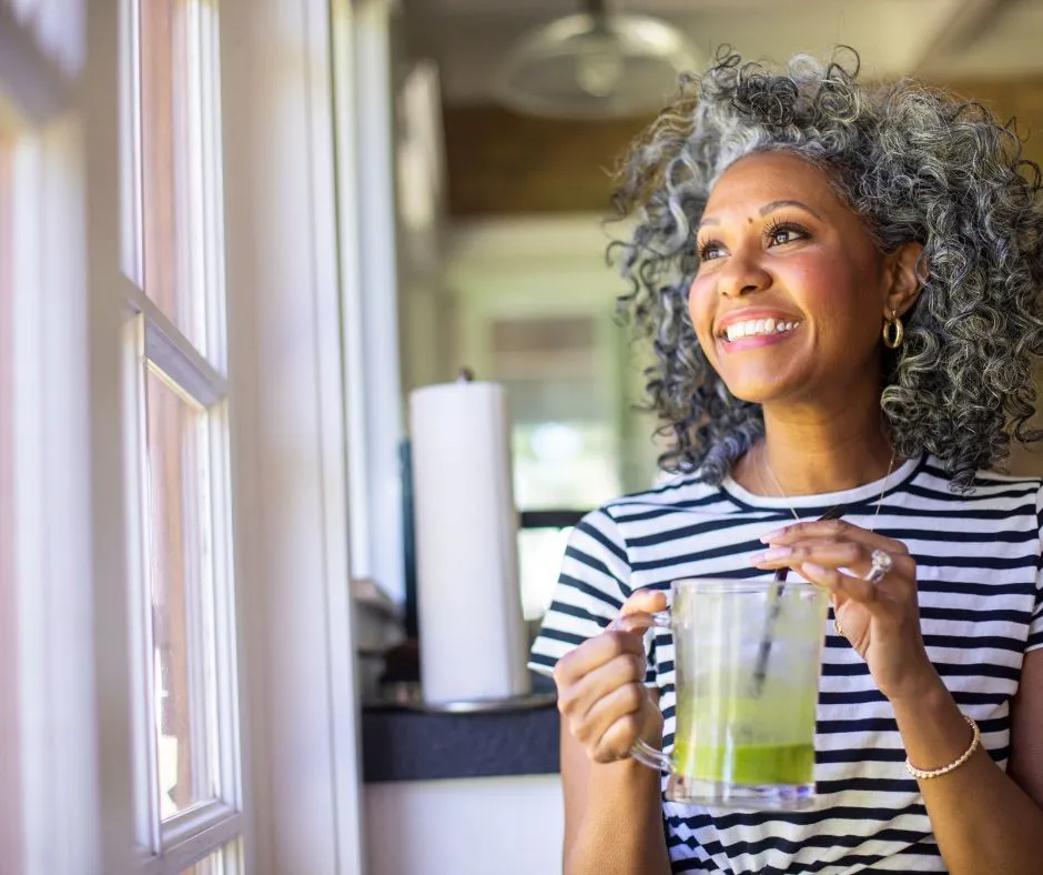 Smiling woman drinking a green beverage by the window