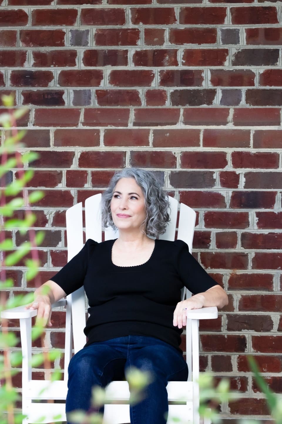 Woman with gray hair sitting against a brick wall