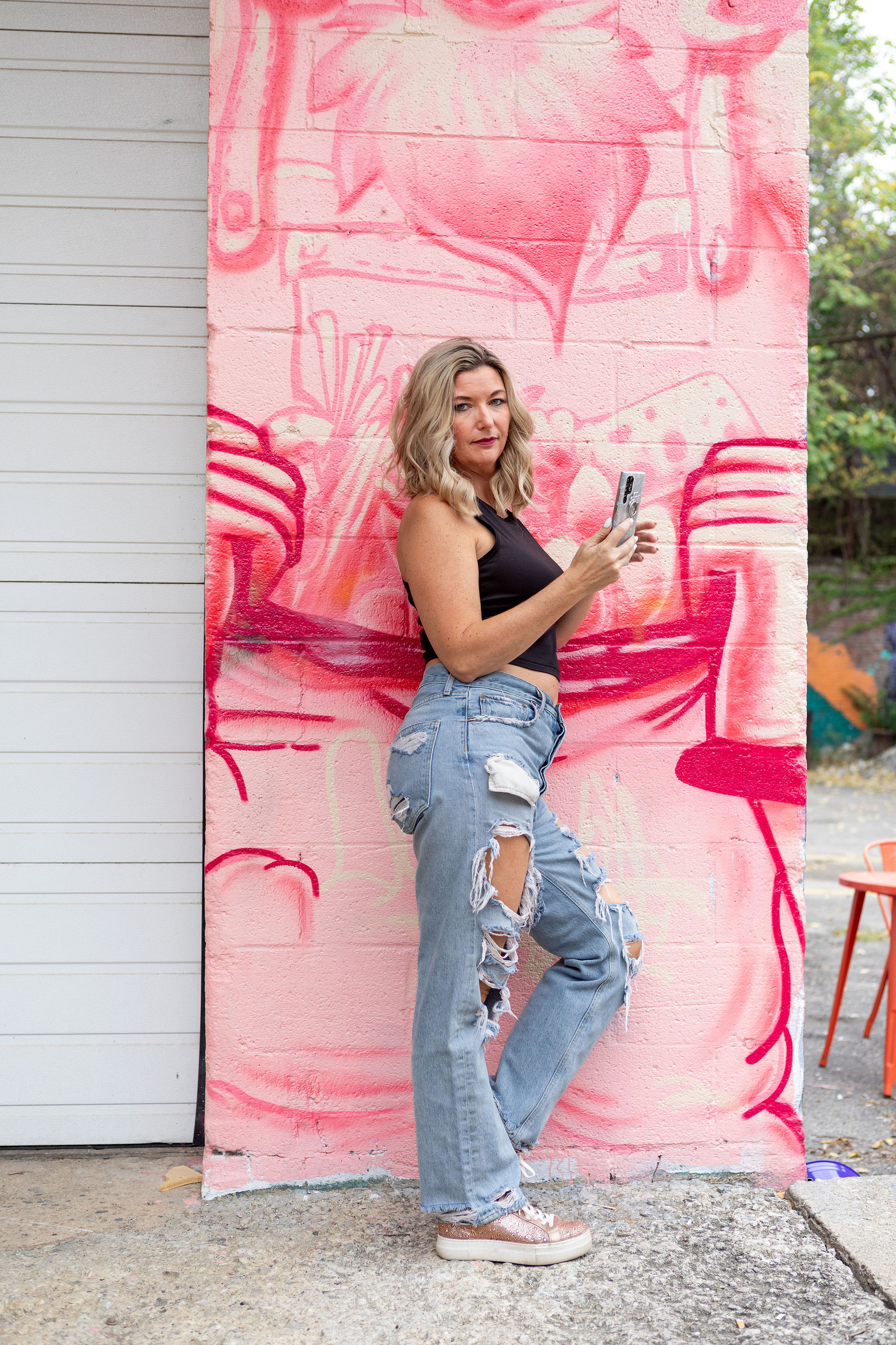 Crissy Conner smiling and holding up her phone in front of a bright pink background