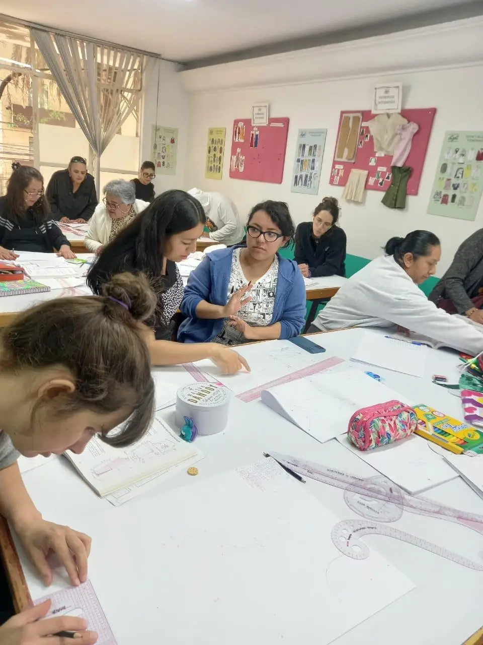Estudiantes y profesora revisando trazos sobre papel con reglas de corte durante el Curso Patronaje Básico de Mujer en Sistema CyC
