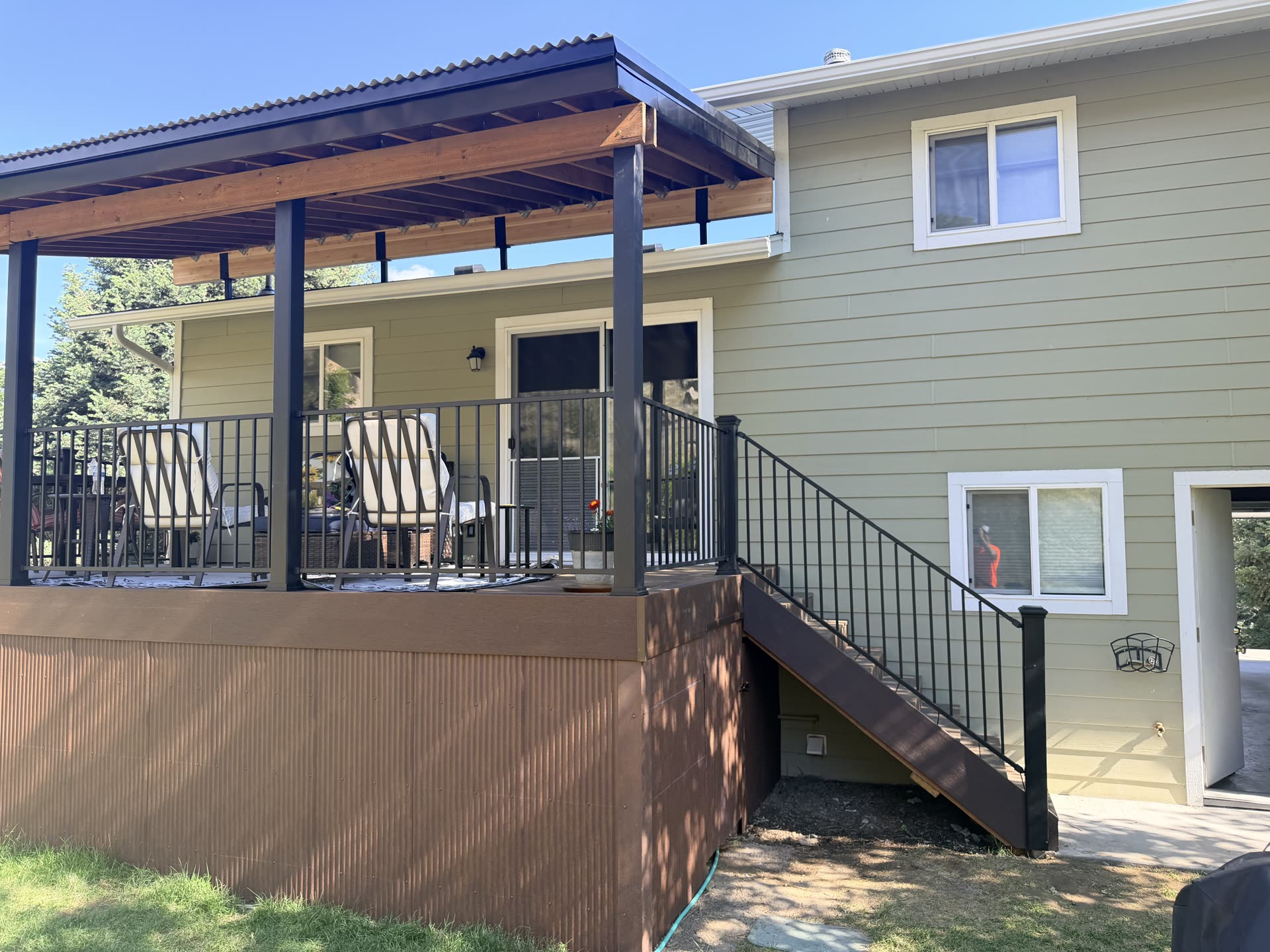 Finished covered deck with a black steel roof over cedar framing and black railing