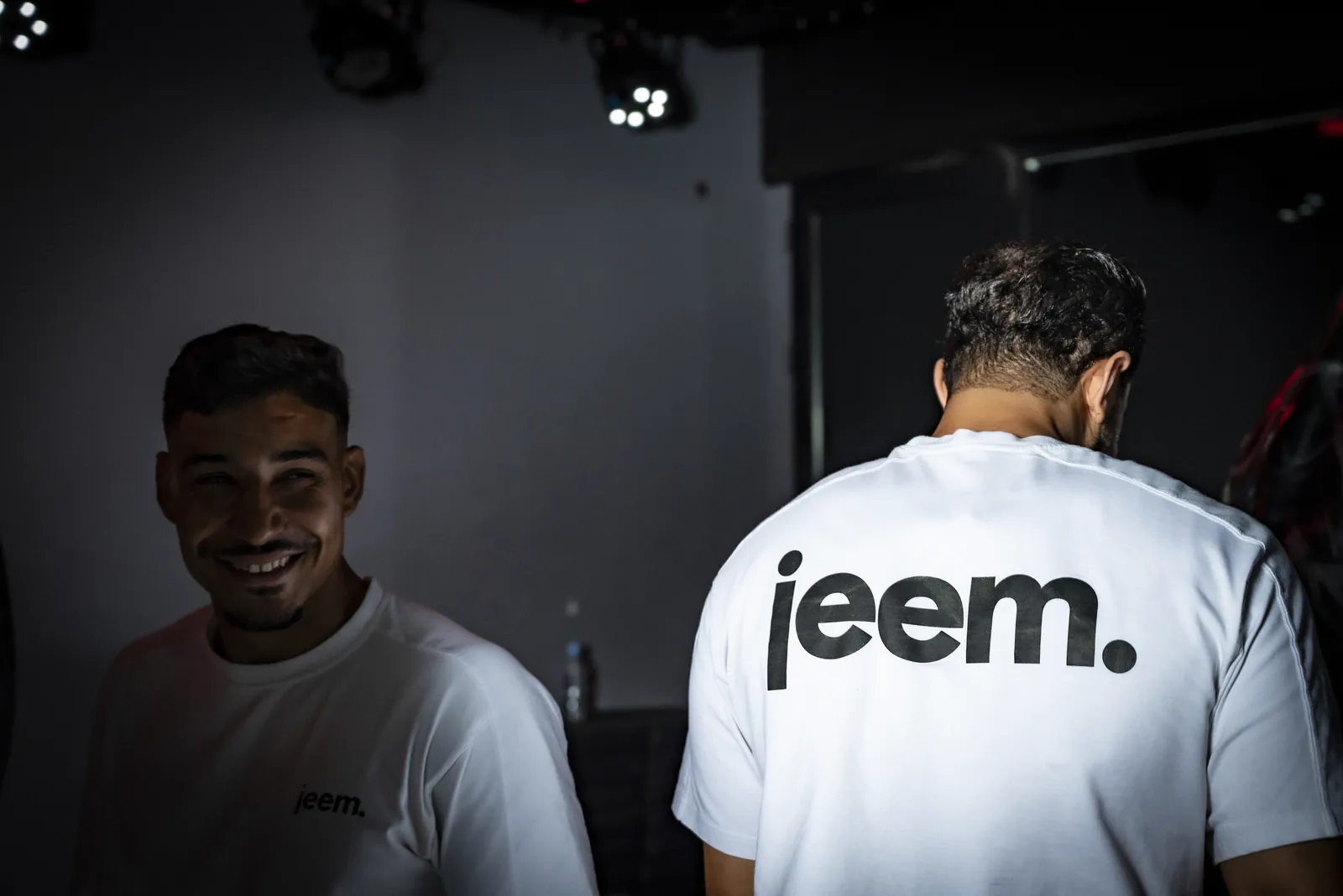 Two jeem coaches in the studio, one smiling at the camera, one showing the jeem logo on his back