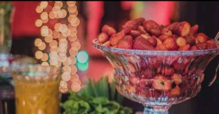 Fruteira com morangos ao lado de uma taça com bebida amarela e hortelã no balcão
