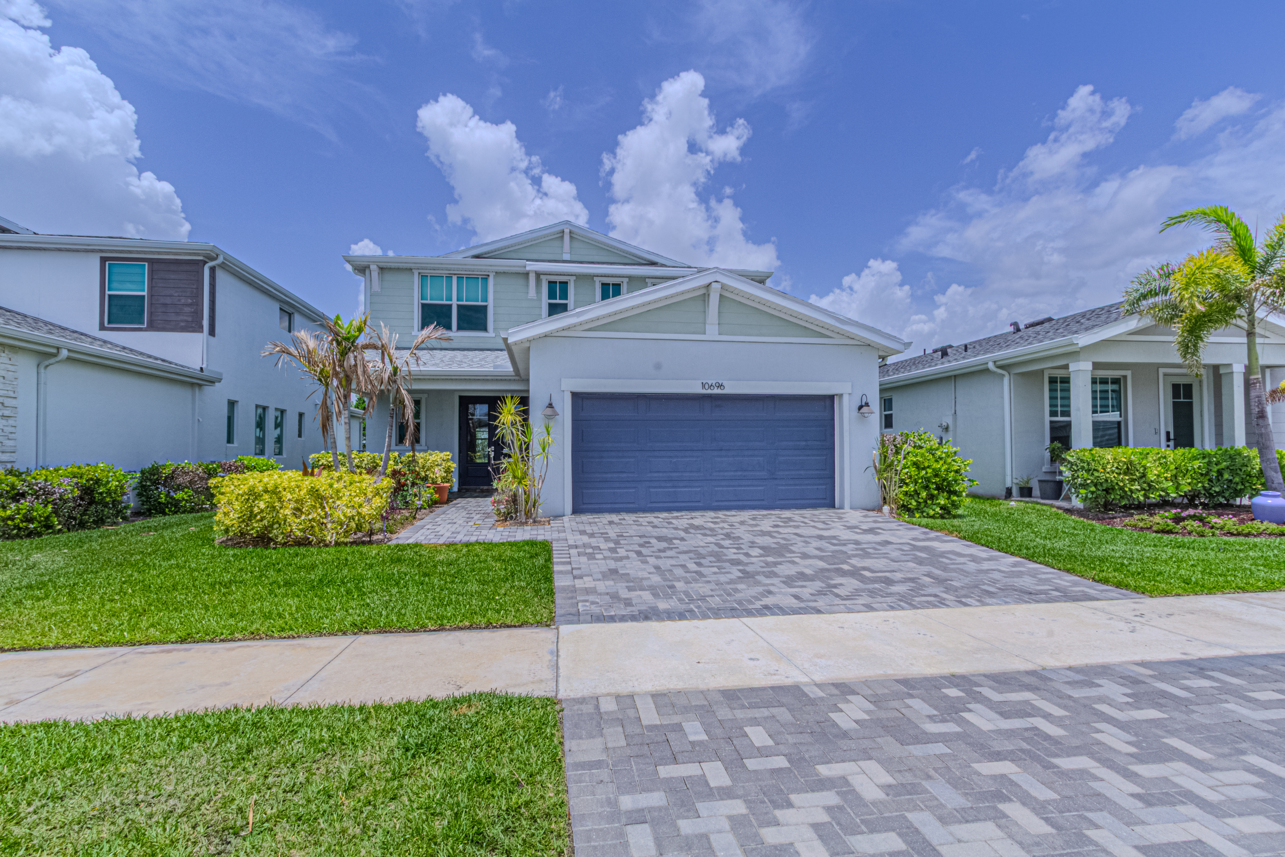 Gray two-story home with a blue garage and paver driveway in daylight