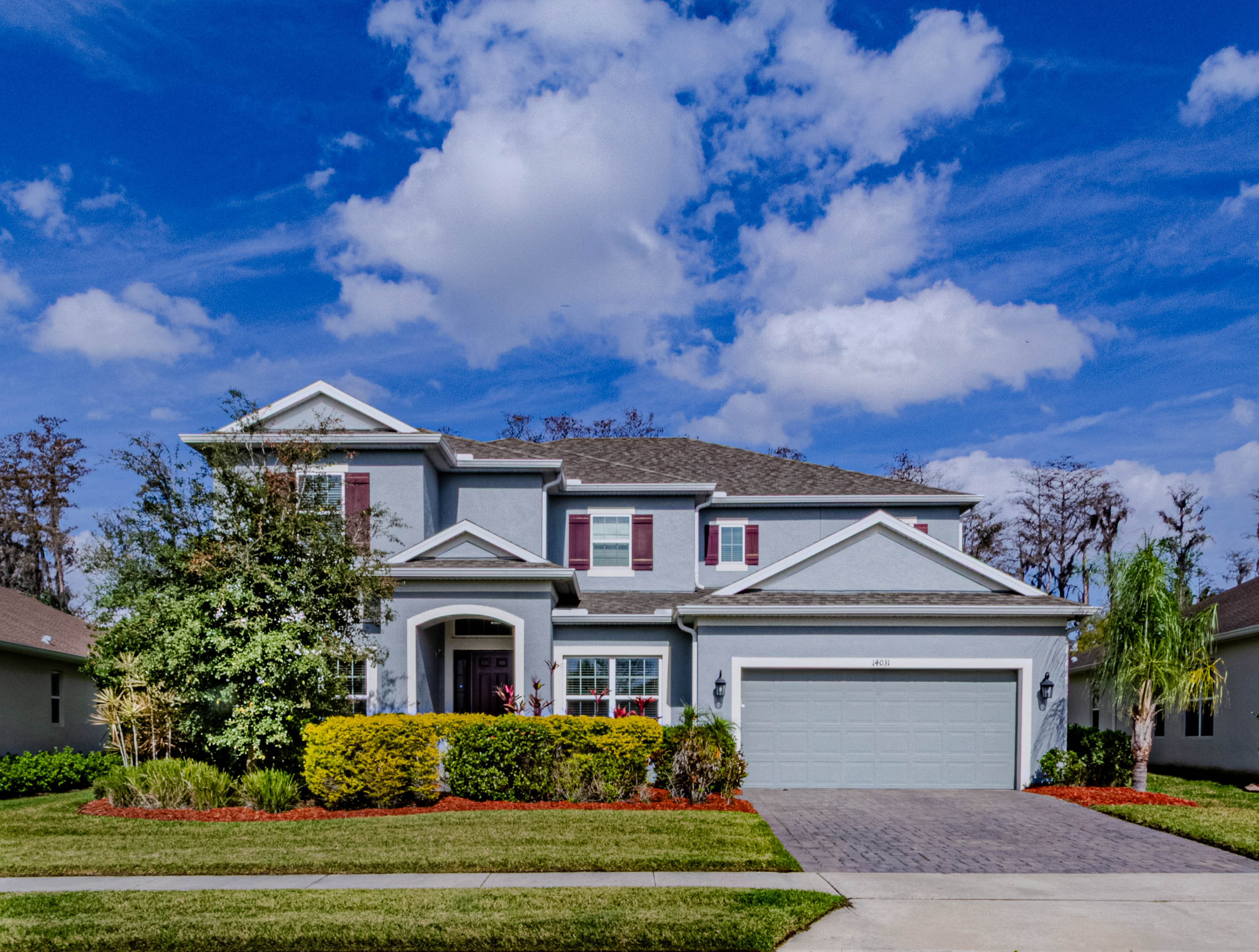 Two-story gray home with burgundy shutters and landscaped front yard