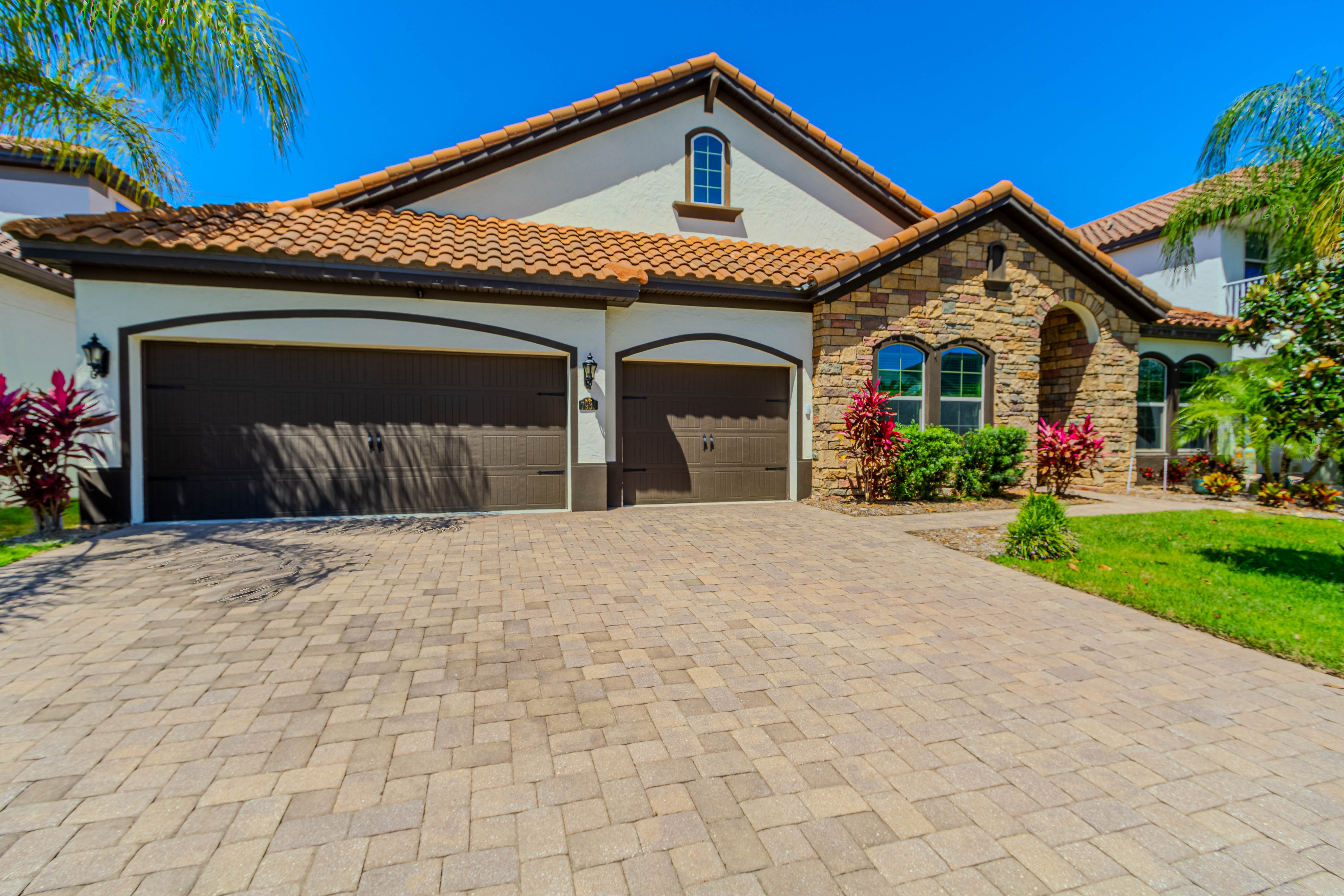 Home with a tile roof, stone facade, palm trees and a three-car garage