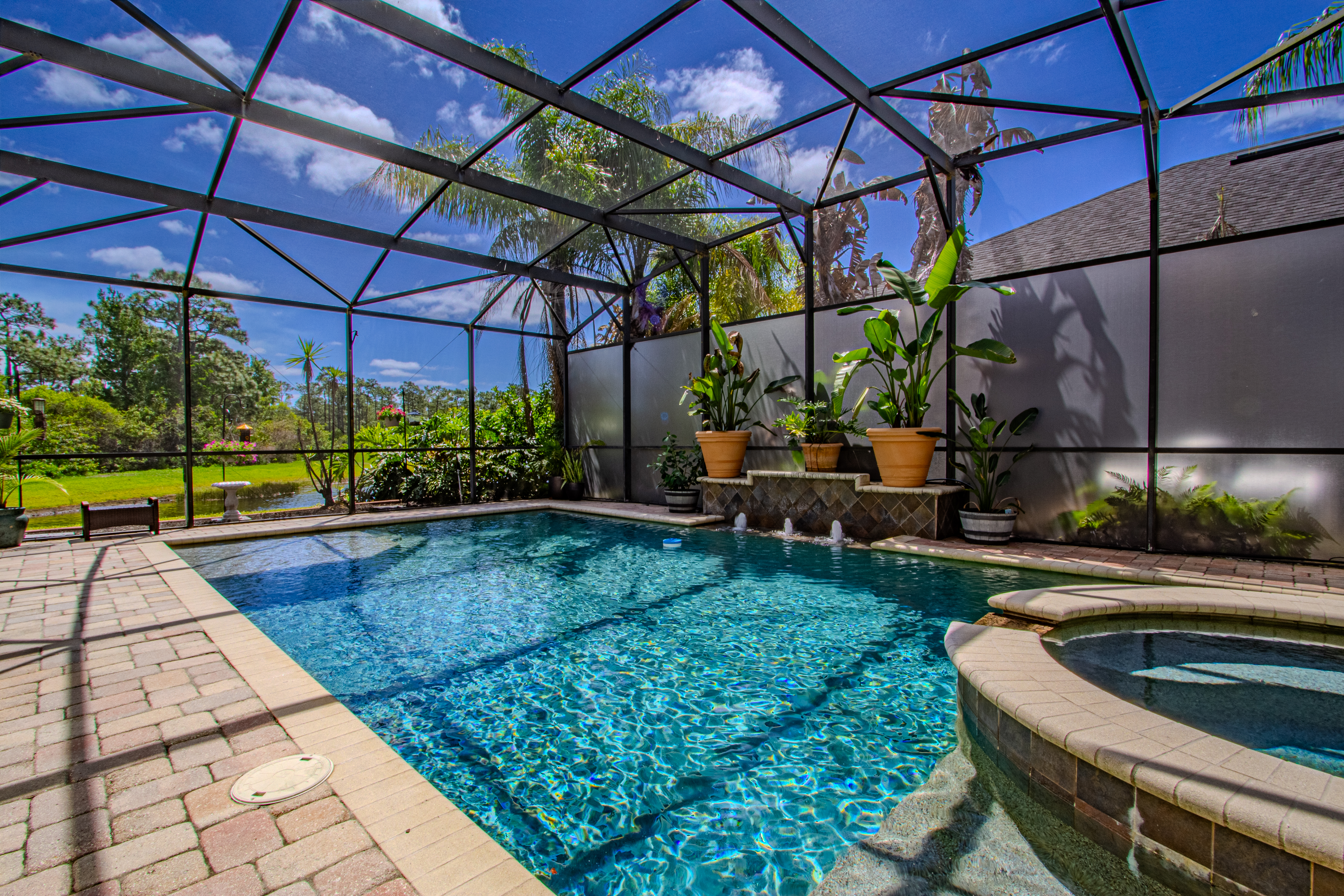 Screened swimming pool and spa with a garden and water view in daylight