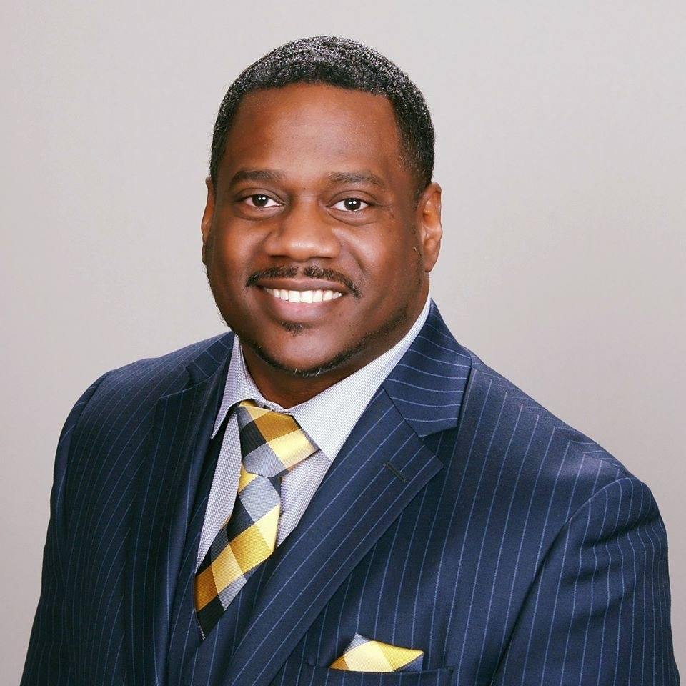 Brandon C. Young in a navy pinstripe suit and gold-striped tie.