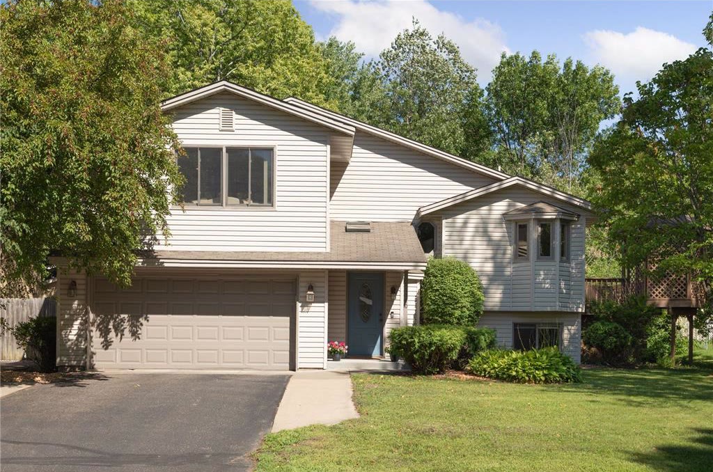 Cream split-level home with a two-car garage, surrounded by mature trees.
